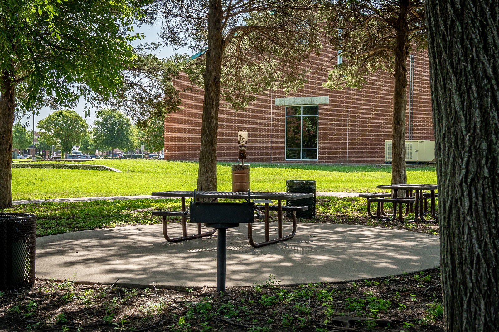 E.L. Tinker Taylor memorial park with green grass, picnic tables, trees, and a walking path. Firehouse in the background.