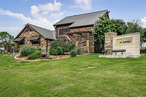 A stone building with a metal roof sits behind landscaping and a sign that reads 