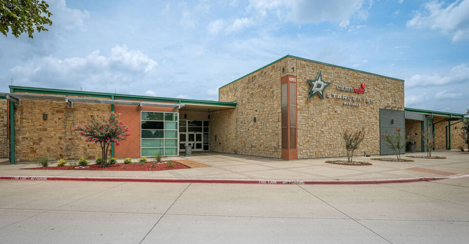 Exterior view of a single-story building with stone facade, glass entrance, and "Stargate" sign on the wall, under a partly cloudy sky.