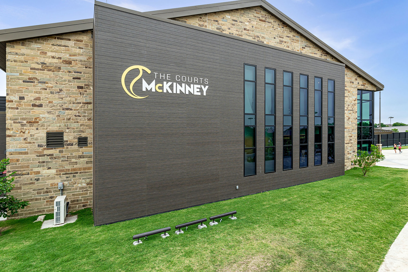 Exterior view of a modern brick and wood-paneled building with tall windows and a sign that reads "The Courts McKinney.