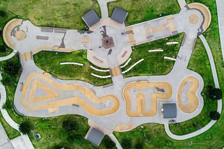 Aerial view of a large outdoor skatepark with winding tracks, ramps, platforms, and scattered green spaces.