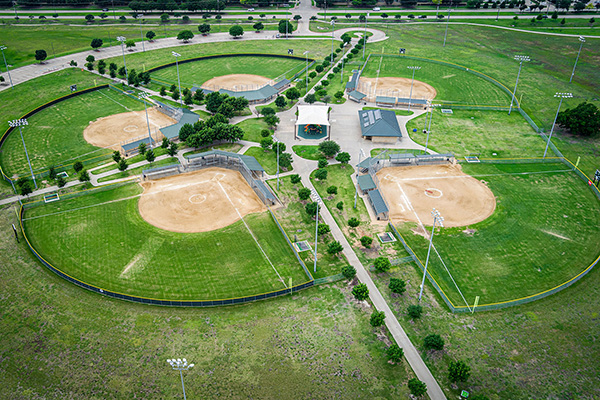 Aerial view of a sports complex featuring four baseball or softball fields arranged in a circular layout around a central building.