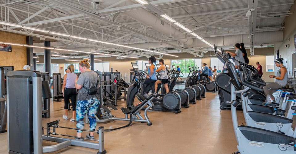 People exercising on cardio machines and weight equipment in a spacious, well-lit fitness center.