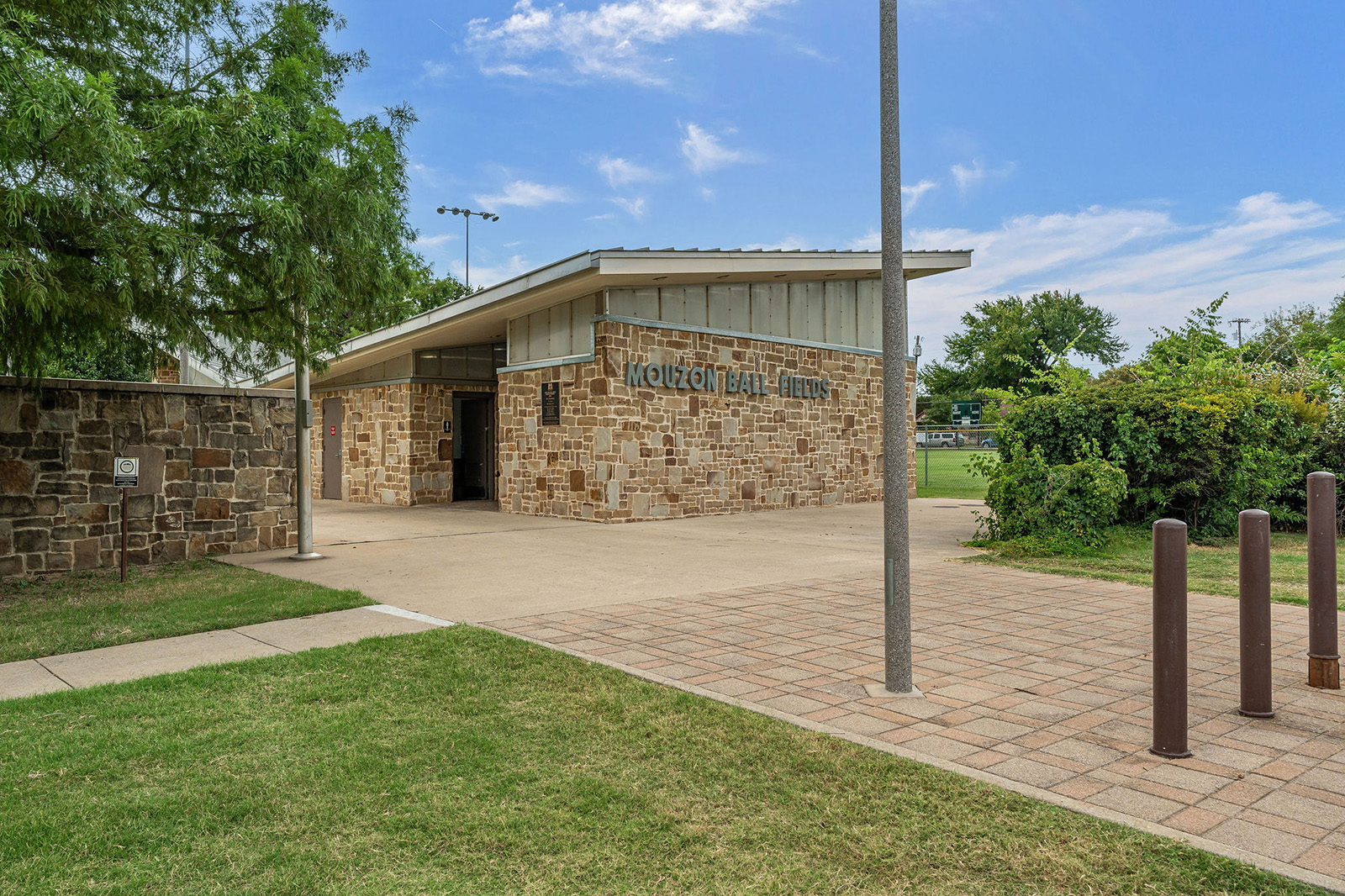 A small stone building labeled "Moulton Hall" stands near a sidewalk, surrounded by grass, trees, and a paved walkway under a clear sky.