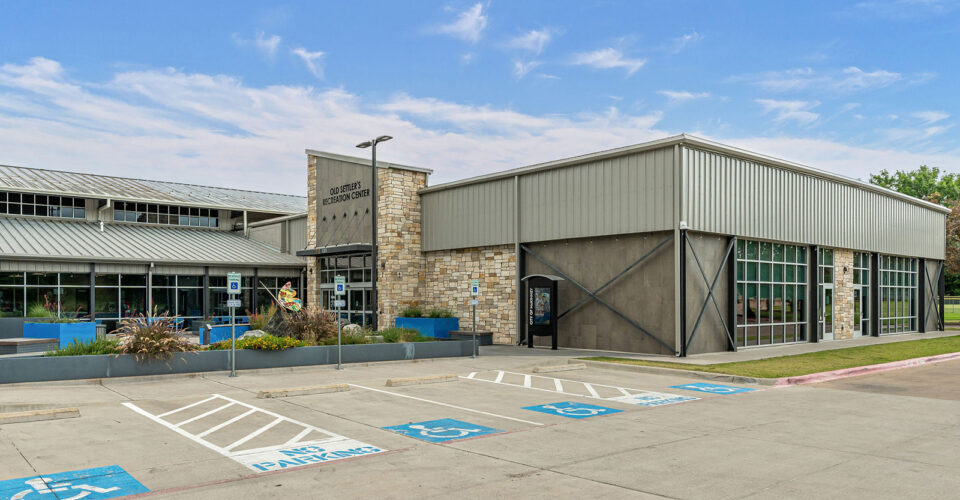 Single-story modern building with stone and metal façade, large windows, and multiple accessible parking spaces in front, under a partly cloudy sky.