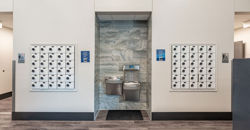 A hallway with two sets of numbered mailboxes on either side of a recessed area containing a water fountain and a bottle filling station.