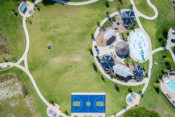 Aerial view of a park with a basketball court, playgrounds, walking paths, shaded areas, and a swimming pool.