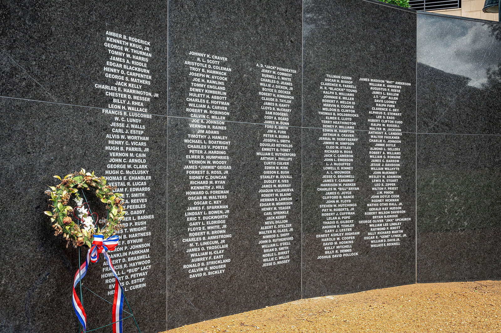 A memorial wall engraved with names, featuring a wreath with red, white, and blue ribbons placed at the base.