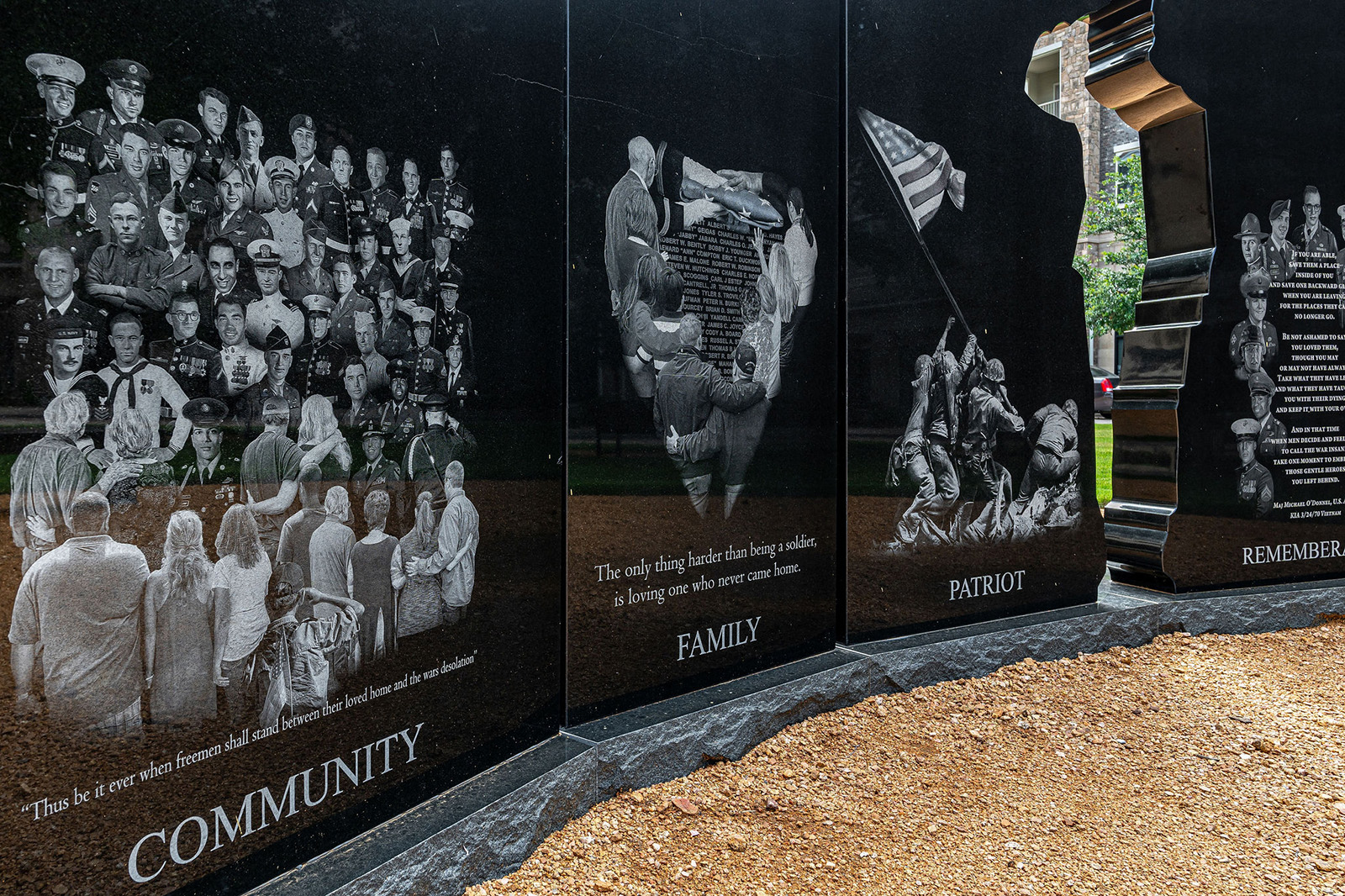 Black stone monument panels display etched images of military personnel and families, with the words "Community," "Family," "Patriot," and "Remember" inscribed at the bottom.