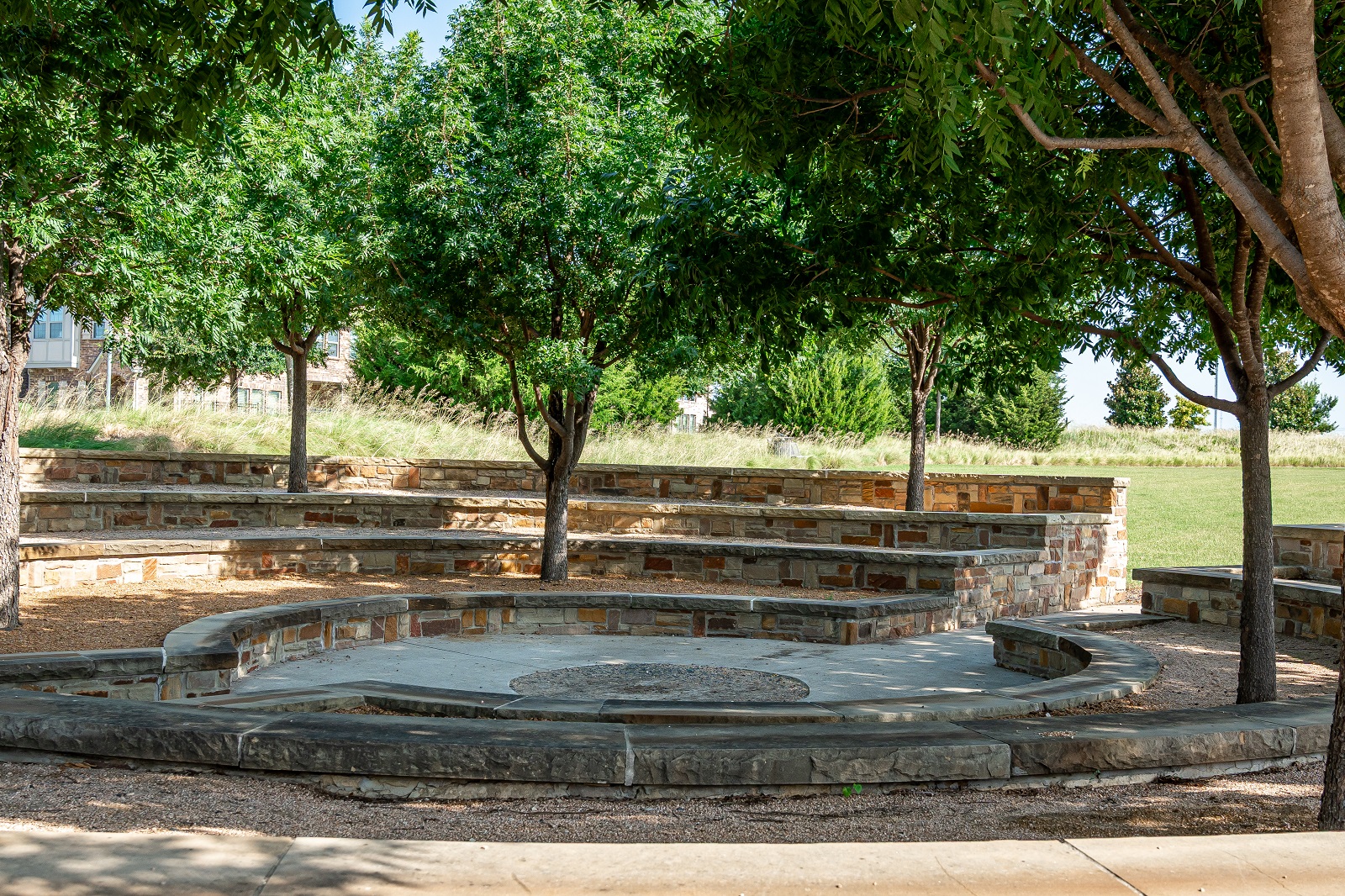 crescent park with stone steps, circular seating with shady trees